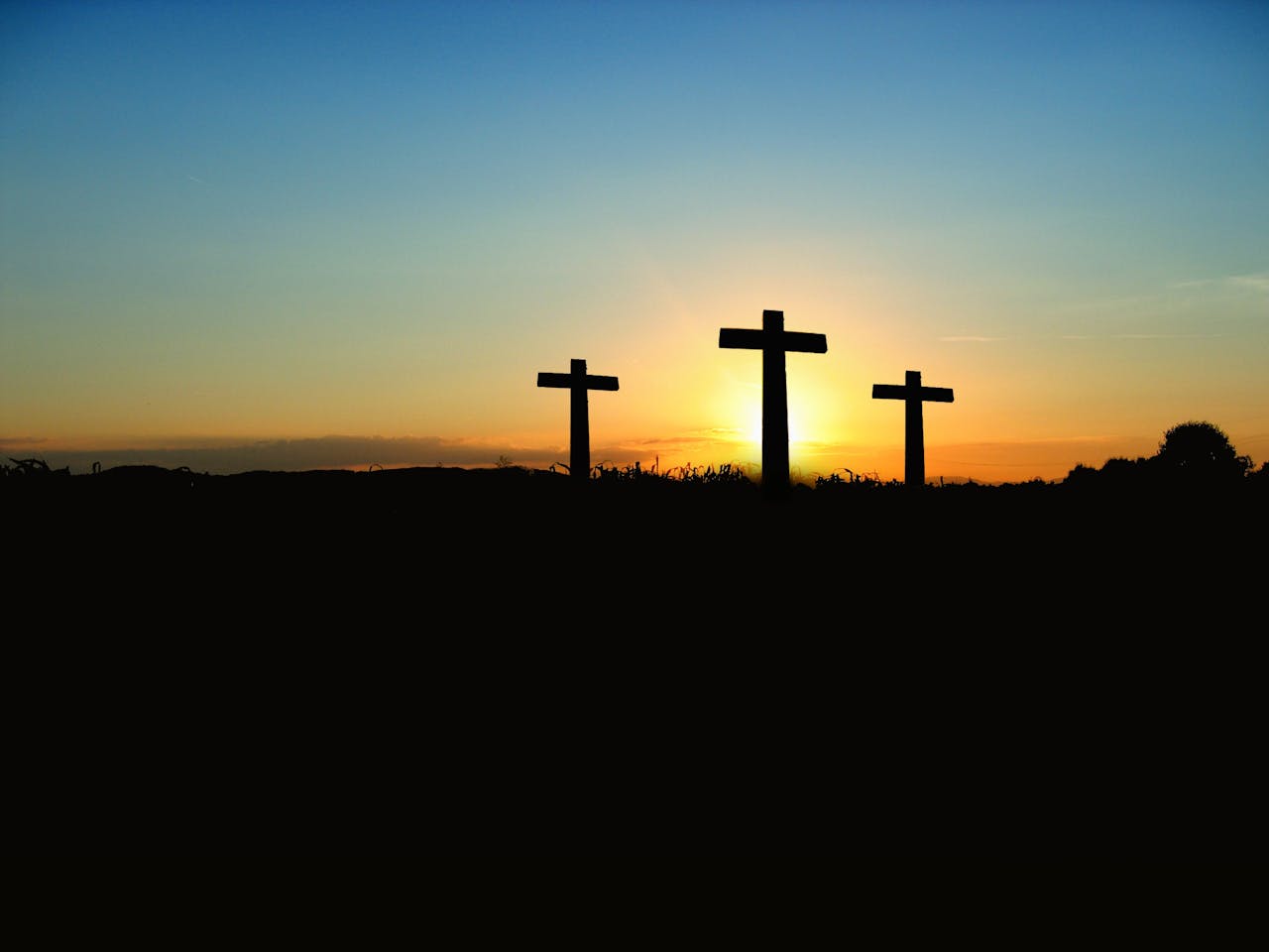 services-01 Silhouette of three crosses against a vibrant sunset sky.
